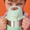 Dziecko trzyma b.box Termos na jedzenie, 335 ml, Spearmint, z pasującym widelcem przymocowanym z przodu. Pojemnik częściowo zasłania twarz dziecka i wyróżnia się na pomarańczowym tle kontrastującym z jego głębokim odcieniem.