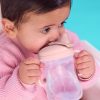 Dziecko w różowym sweterku siedzi na turkusowym tle, trzymając i pijąc z kubka z miękkim ustnikiem 240 ml, Blush. Jego podwójne uchwyty są mocno trzymane. Ciemne włosy dziecka są starannie uczesane, gdy spogląda w bok.
