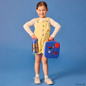 Superman by bbox lunchbox lifestyle dziewczynka stoi i trzyma w lewej ręce lunchboxa, a w prawej bidon termiczny ze słomką 350ml w tym samym motywie