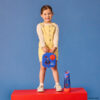 Superman by bbox mini lunchbox lifestyle dziewczynka stoi na podwyższeniu trzyma w rękach mini lunchboxa, obok jej lewej nogi stoi butelka tritanowa ze słomką 600 ml z motywem supermana