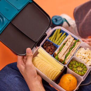 Zorganizowany lunchbox b.box trzymany w dłoniach z wypełnionym niebieskim wkładkem silikonowym bento